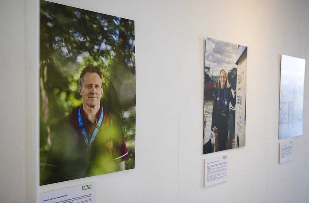 Two portraits of NHS staff. On the left, a man in red scrubs stands in a wood, dappled light falling through the trees. On the right, a woman in blue stands by a boating dock