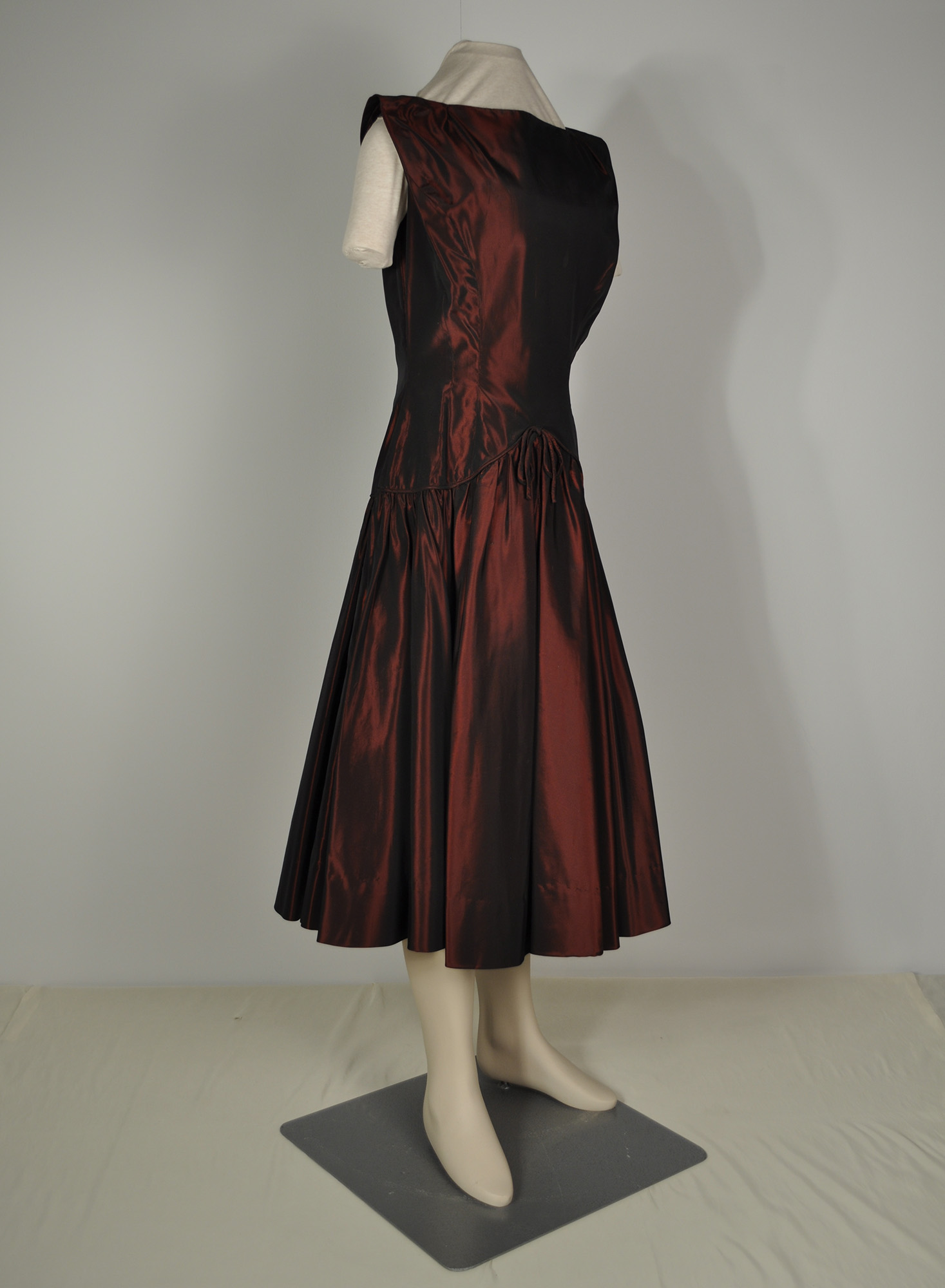 A woman's cocktail dress in the fit and flare style, made from burgundy taffeta. It has a high neckline and short sleeves