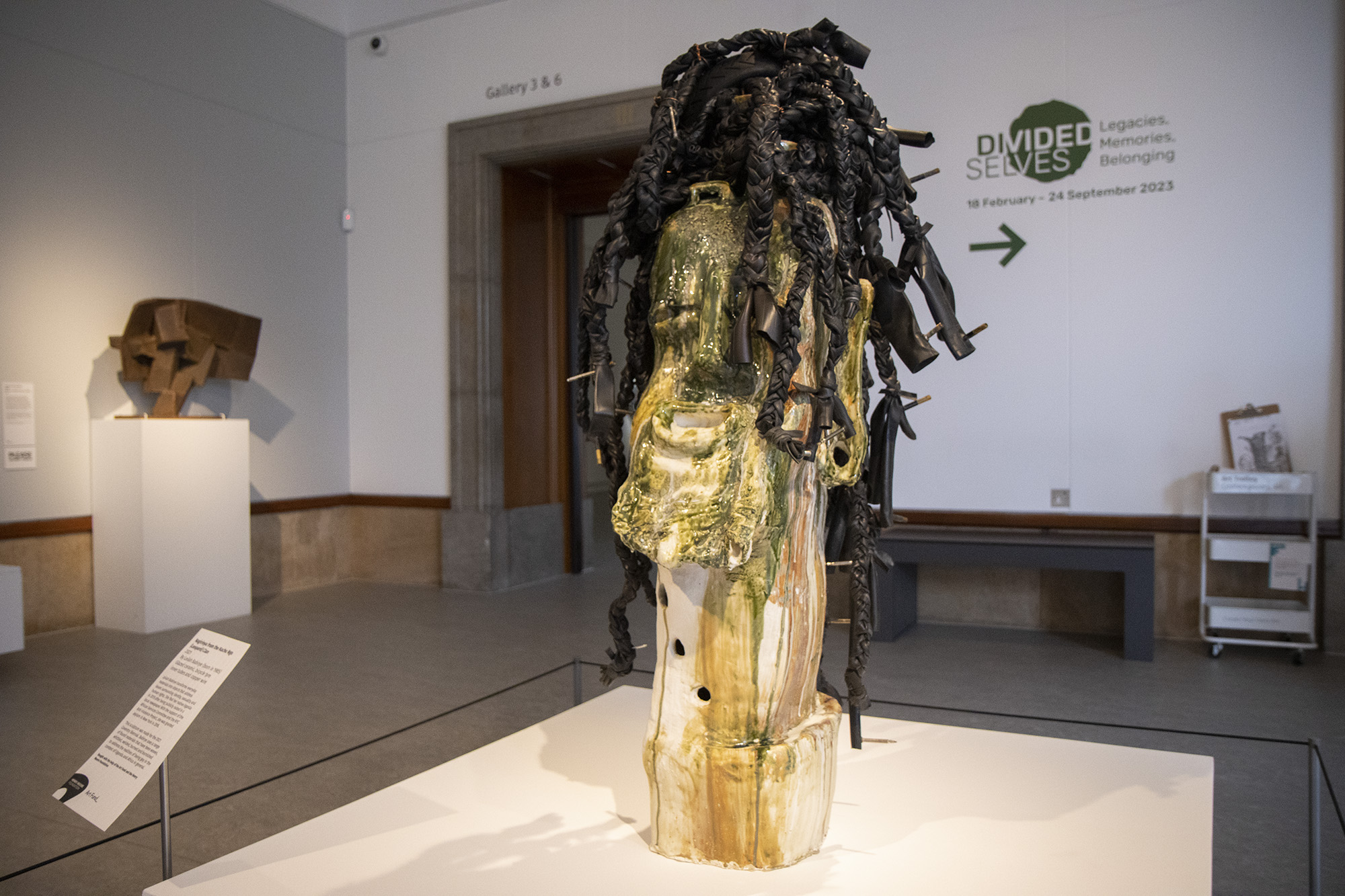 Leilah Babirye's sculpture "Nagirinya from the Kuchu Ngo (Leopard) Clan" on display at the Herbert Art Gallery & Museum. The sculpture is a large, white ceramic head painted in green and yellow tones, with braided hair made from waste rubber tubing