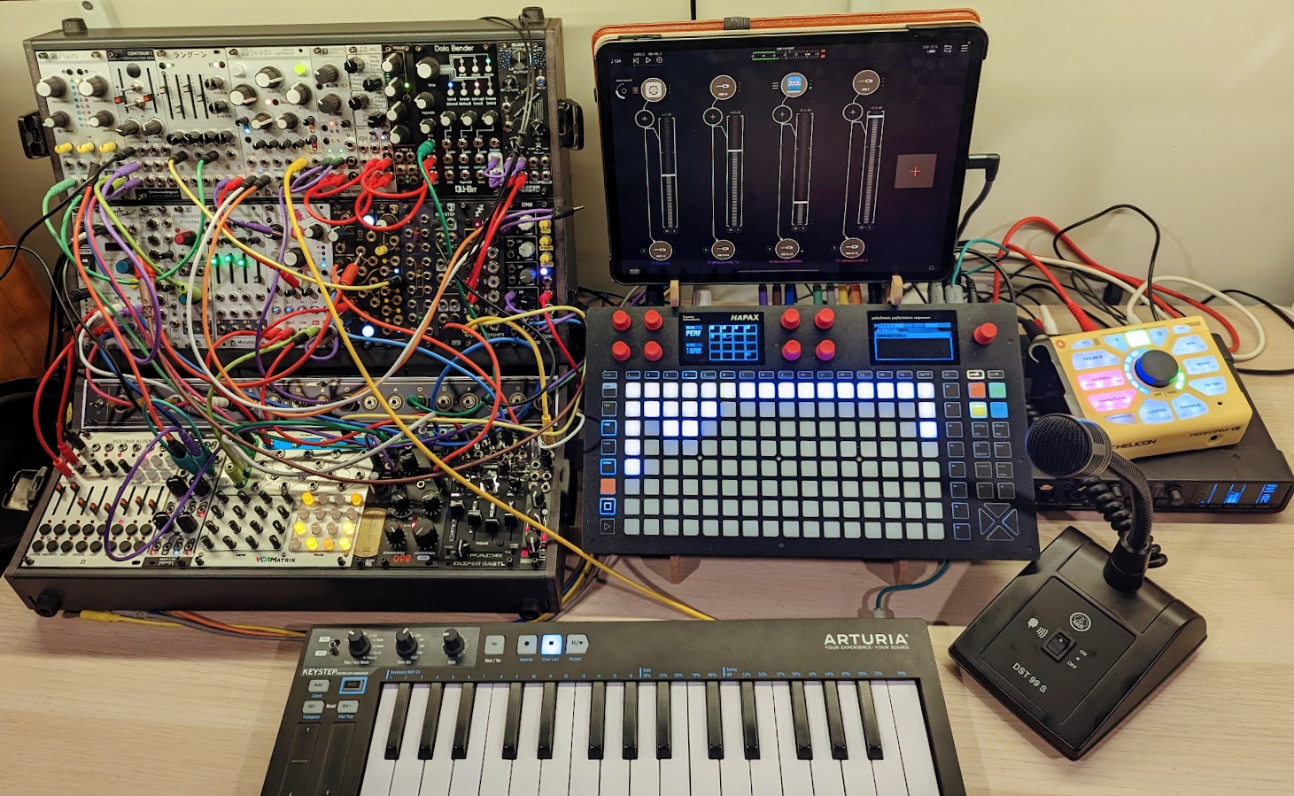 A modular synth set up on a desk with multicoloured cables, a microphone and a keyboard