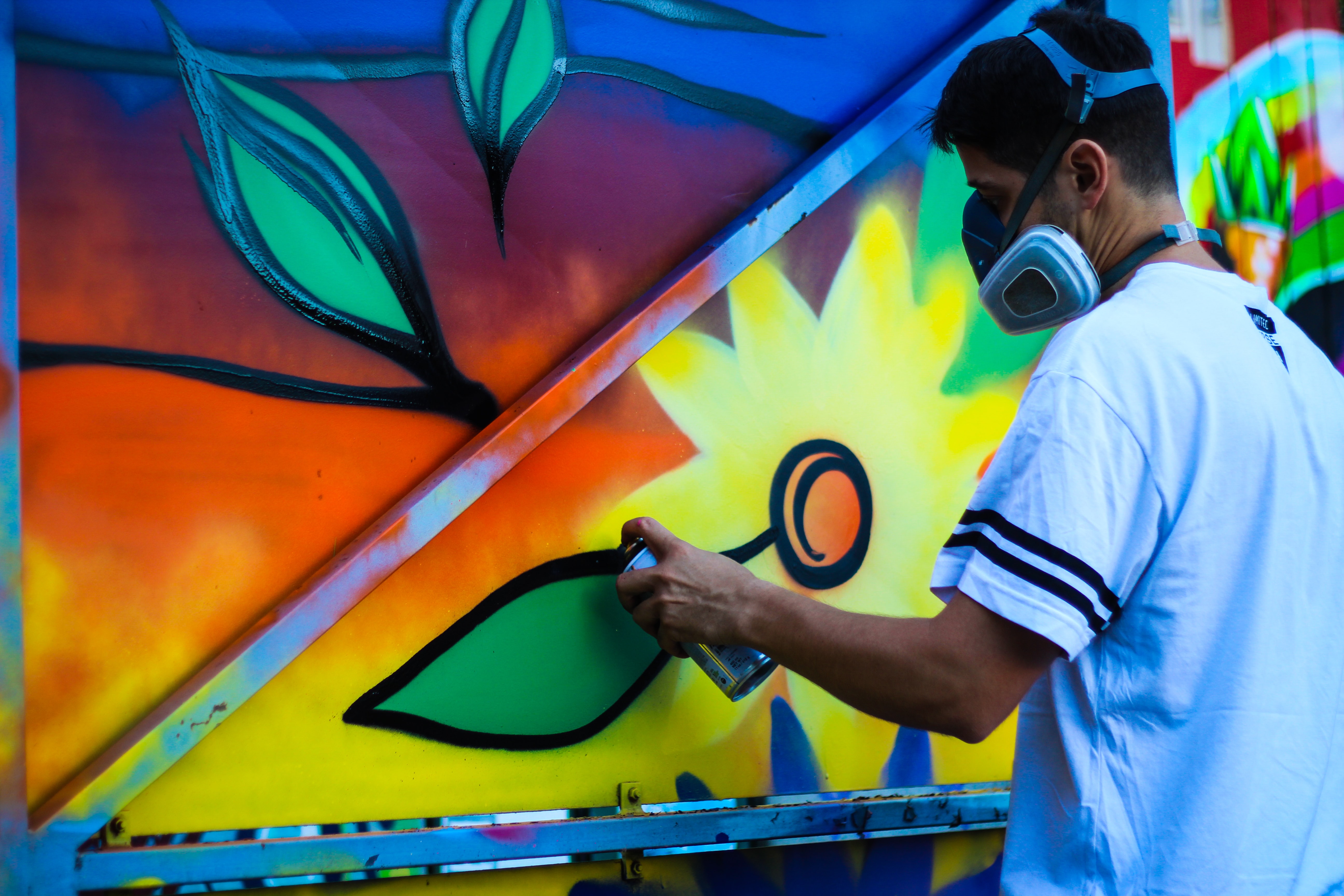 A man in a mask painting a floral street art mural