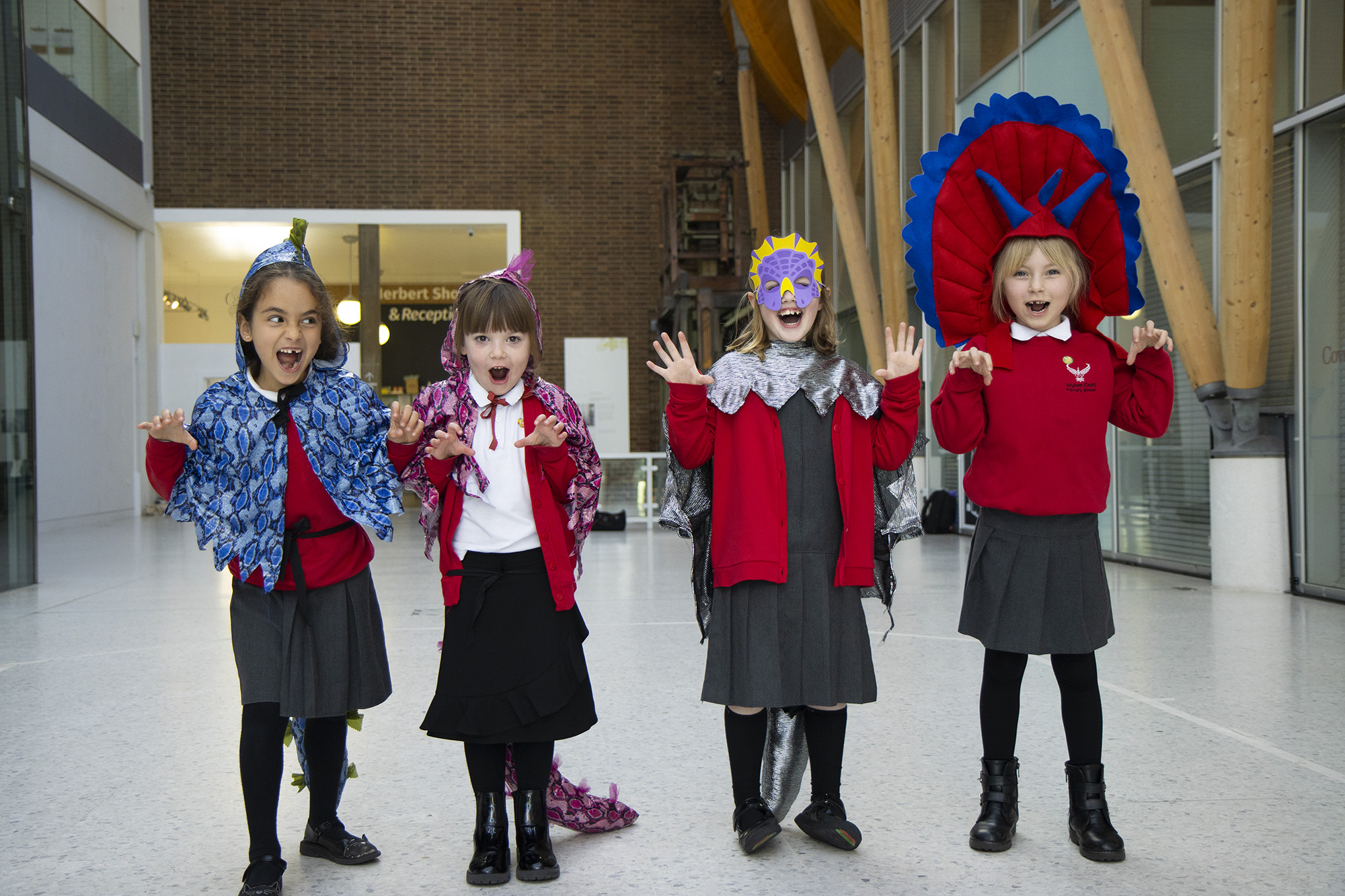 A group of children dressed up in hand-made dinosaur costumes, roaring with their hands clawed in front of them