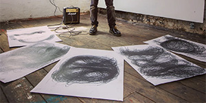 A set of abstract sketches laid out on a wooden floor around Gerald Curtis' feet