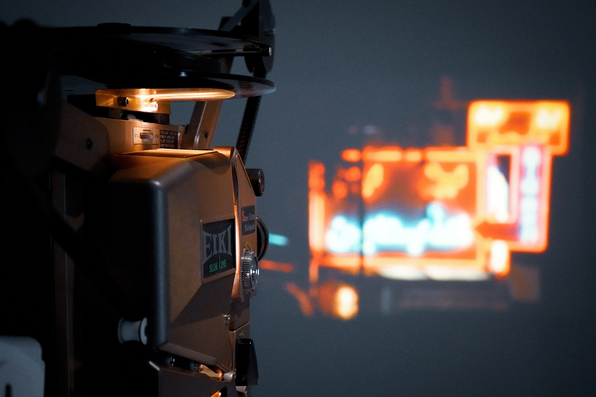 A projector in the foreground, with a scene from a film featuring bright neon lights projected in the background.