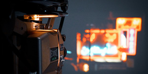 A projector in the foreground, with a scene from a film featuring bright neon lights projected in the background.