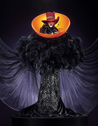 Daniel Lismore sculpture featuring a full-length black skirt, ruffled black top and cape, a bright orange dome around the neck and a wide-brimmed red hat