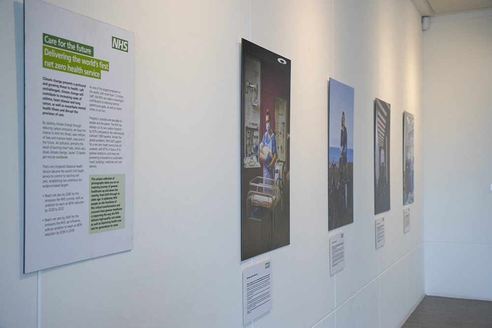 Portrait photos of NHS staff on display in the Herbert Art Gallery, alongside an info panel reading, "Care for the Future: Delivering the world's first net zero health service"