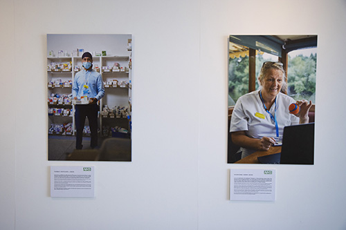 Two photo portraits of NHS staff. On the left, a man in a patka and blue shirt stands in a pharmacy, holding a box of medicines. On the right, a woman in white scrubs sits at a laptop computer, holding up an orange tennis ball