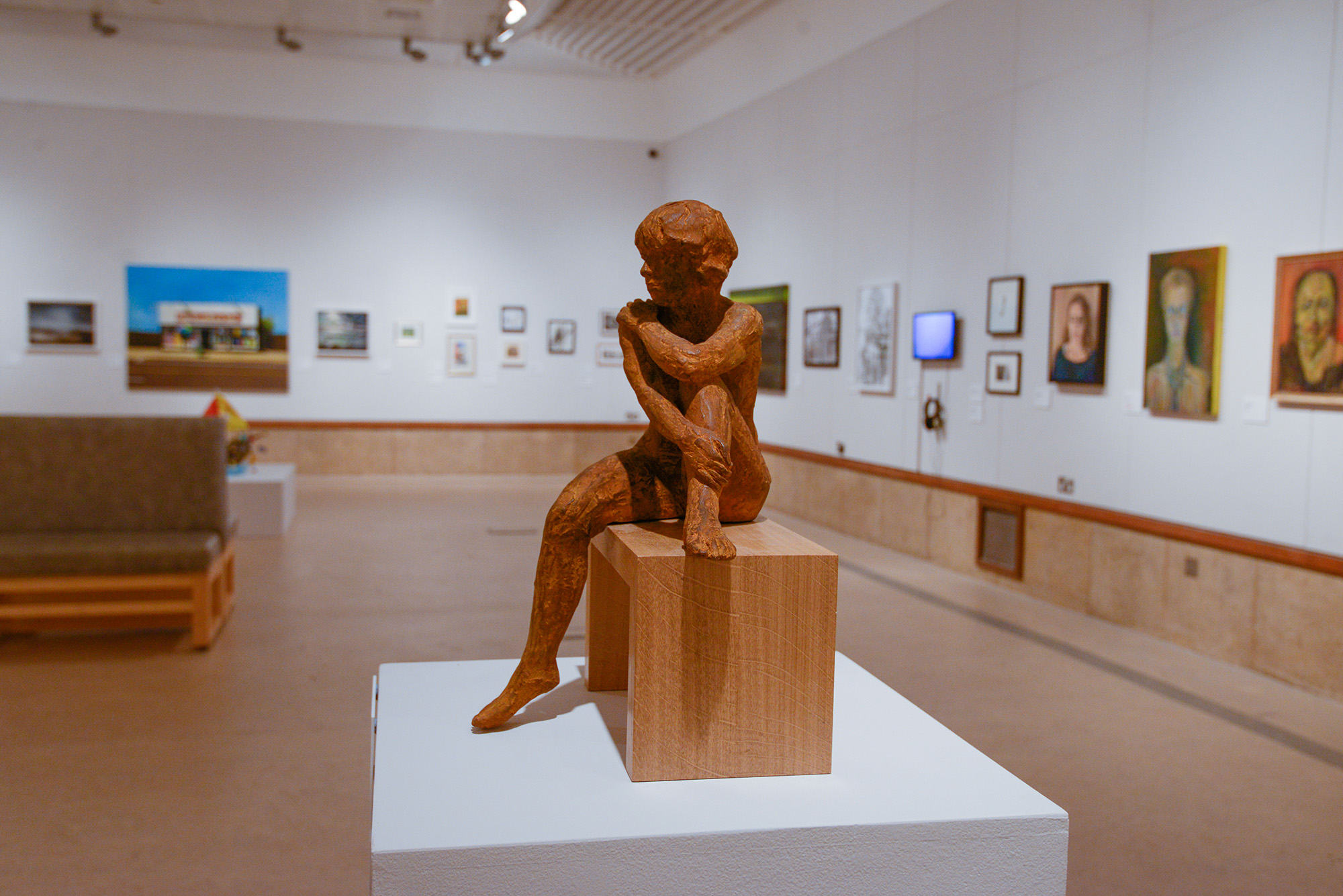 A photo from the Coventry Open 2020 exhibition showing a small figure sculpture on a plinth, surrounded by paintings and drawings hanging on white walls