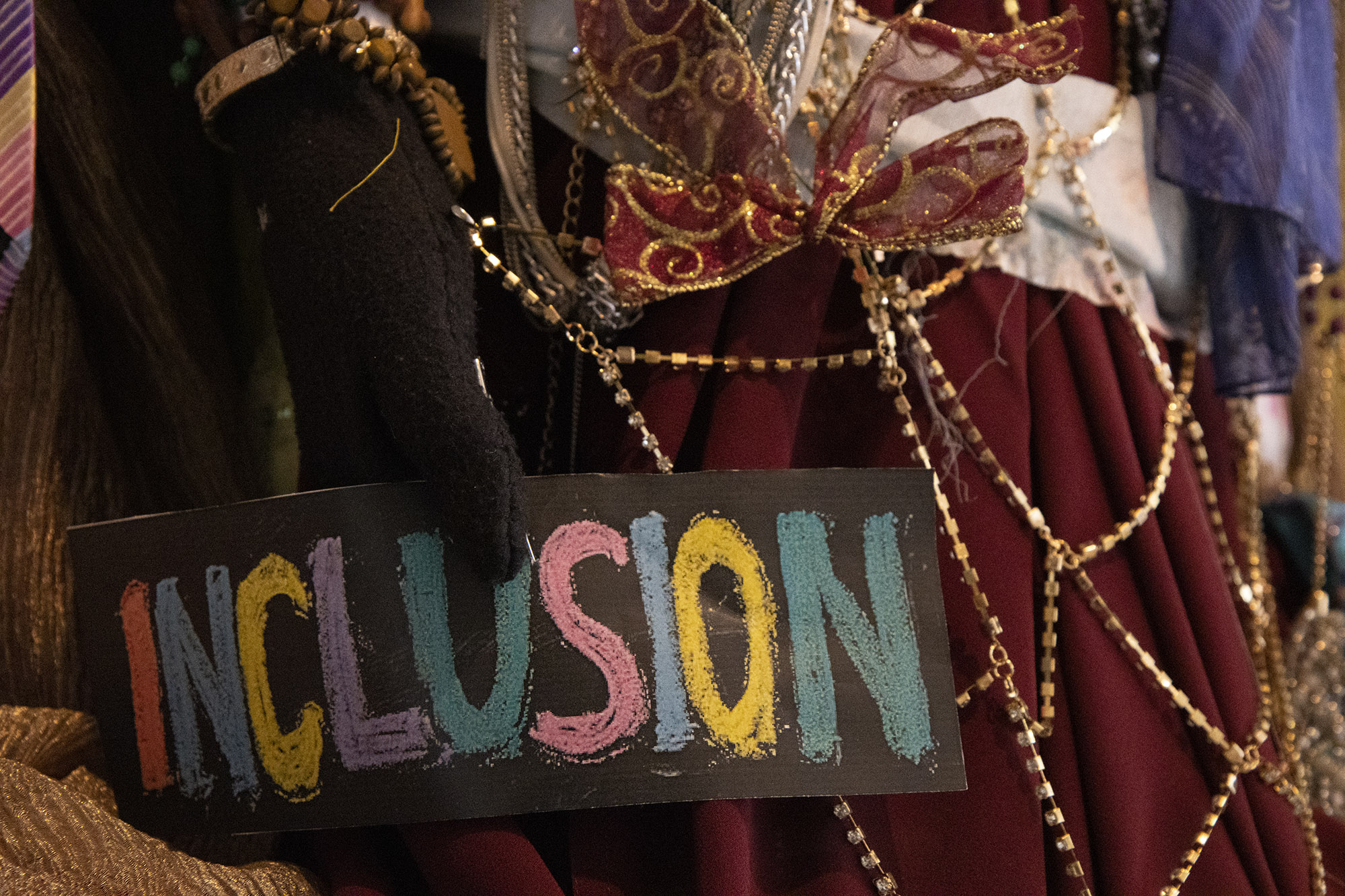 The word, "INCLUSION" written in coloured chalk on black card is fixed to crimson fabric, decorated with gold diamanté chains and a red and gold ribbon bow.