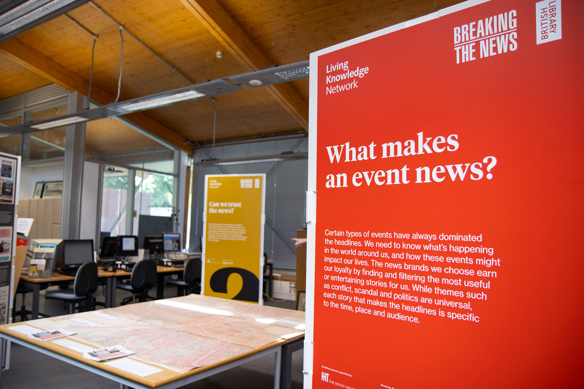 A photo of the Breaking the News exhibition in the Herbert's History Centre, with a large display board in the foreground reading, "What makes an event news?" Behind that is a table covered with a map of Coventry, and in the background is another display board with the headline, "Can we trust the news?"