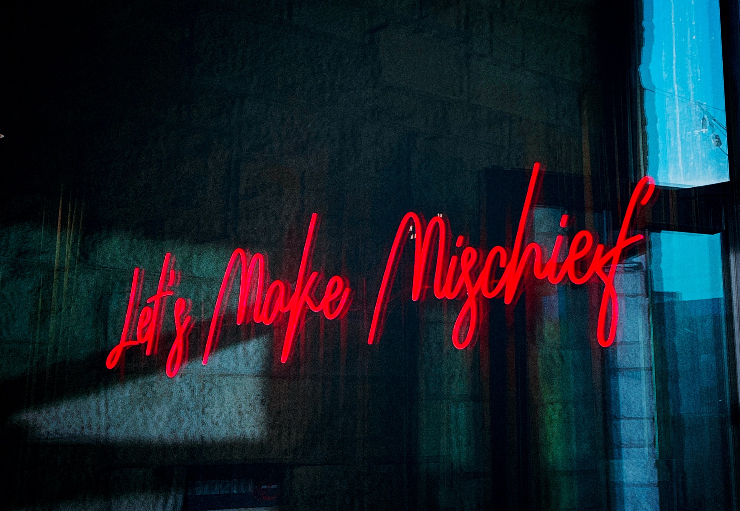 Neon text reading, "Let's Make Mischief" against a dark background
