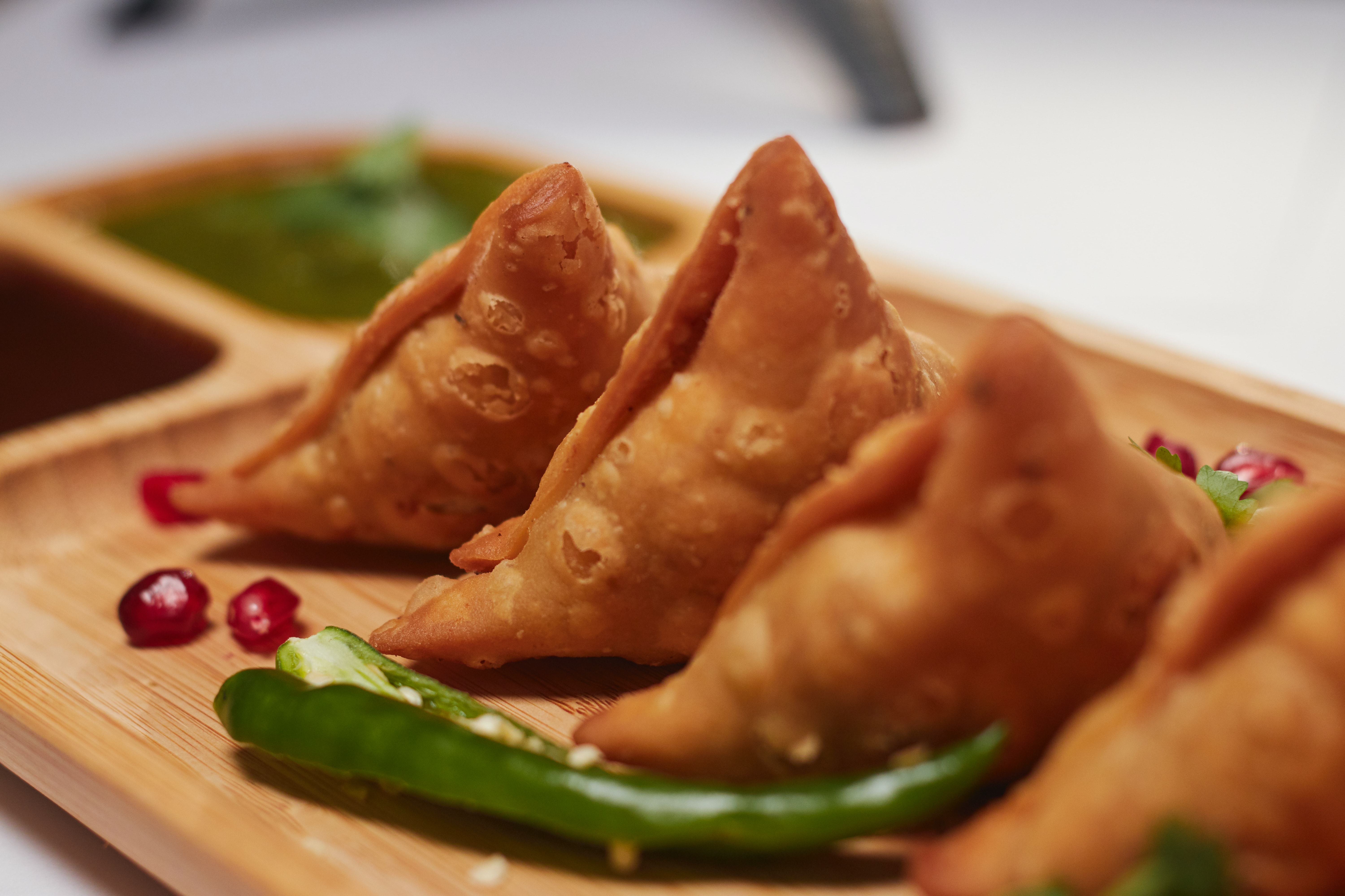 Four samosas served with herbs and chilis on a small wooden tray