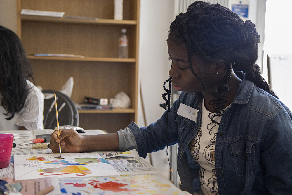 A photo of a girl sitting at a table painting with coloured paints