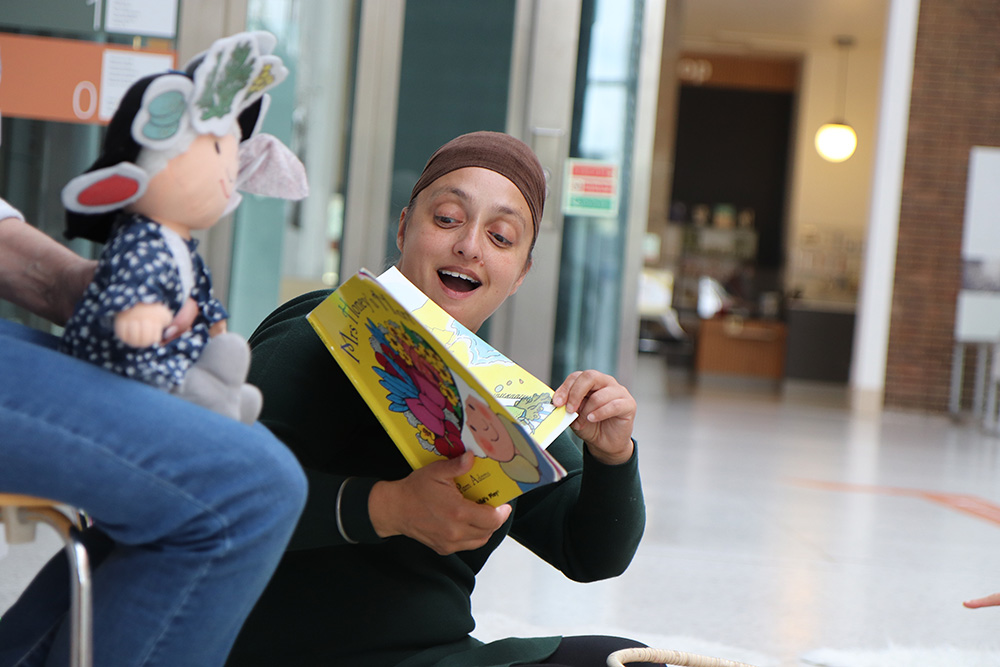 A member of Herbert Learning staff reading a picture book out to a group of children in the Herbert's covered court