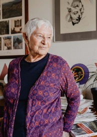 A more recent colour photograph of Hannah Miley leaning against a desk piled with books and papers