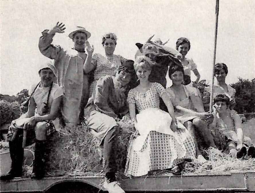 Members of Stoke St Michael youth club in sitting on hay bales at a carnival, dressed in peasant-farmer style costumes with a pantomime cow