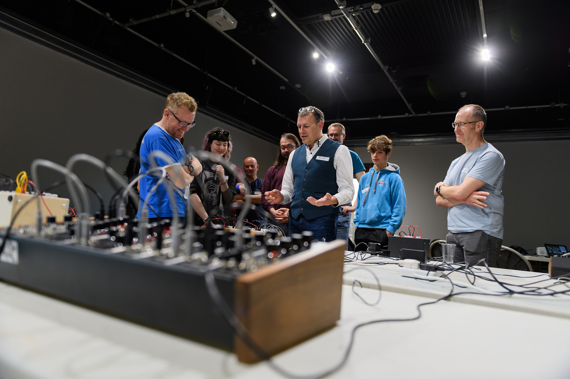 Rick Holt from Frequency Central leading a modular synth workshop at the Herbert in 2022. There is a group of people gathered around him and a synth on a table in the foreground in front of them.