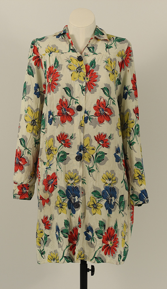 A long, buttoned housecoat, worn like overalls for women. It is white with a floral print