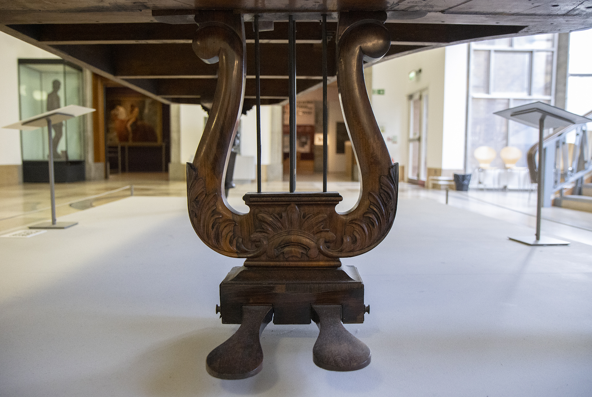 A close up of the harp-like wooden structure which the piano pedals are attached to, with curved, foliage-like carvings.