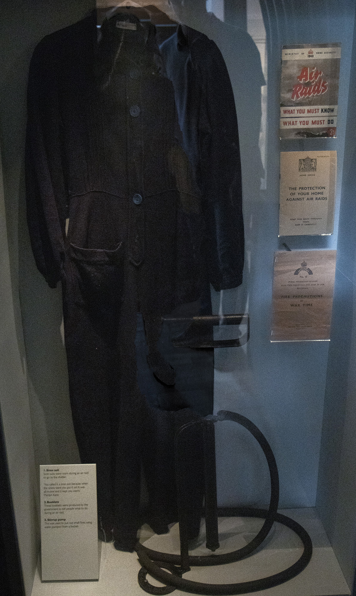 A dark blue siren suit on display next to Air Raid information booklets in the Herbert's History Gallery