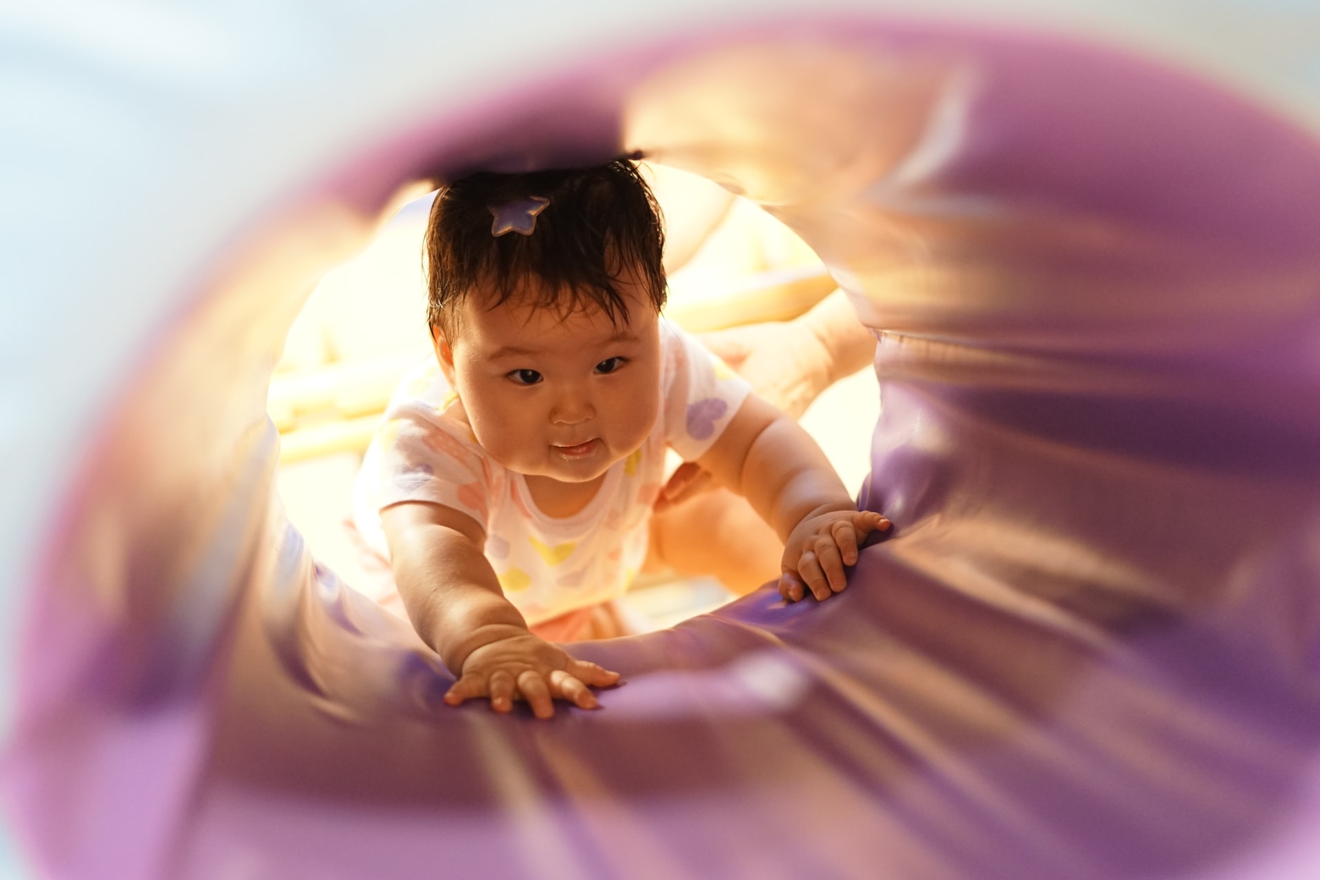 A photo of a baby peering inside a pink play tunnel