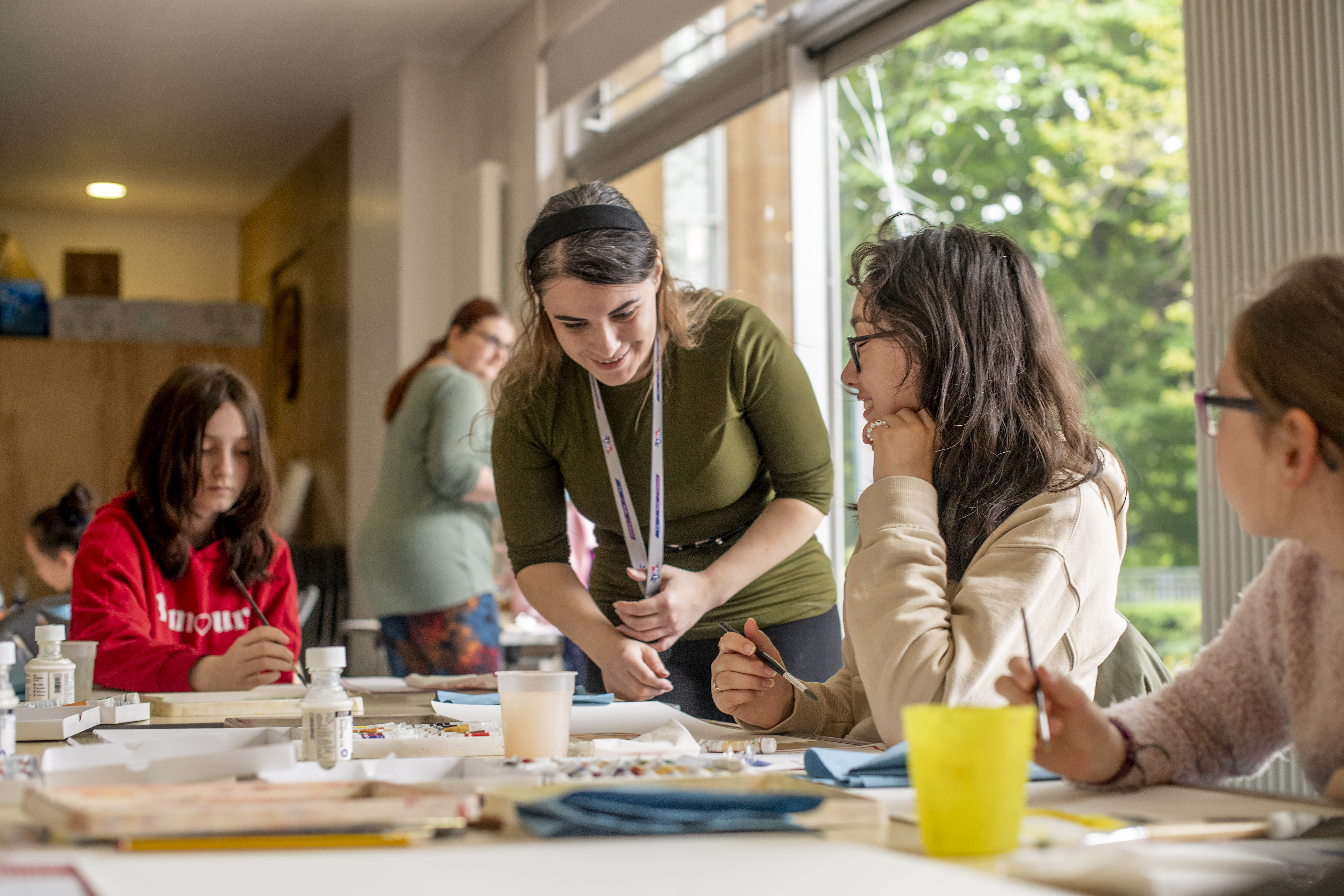 A photo of a practitioner helping a group of teenage girls who are sitting around a table painting