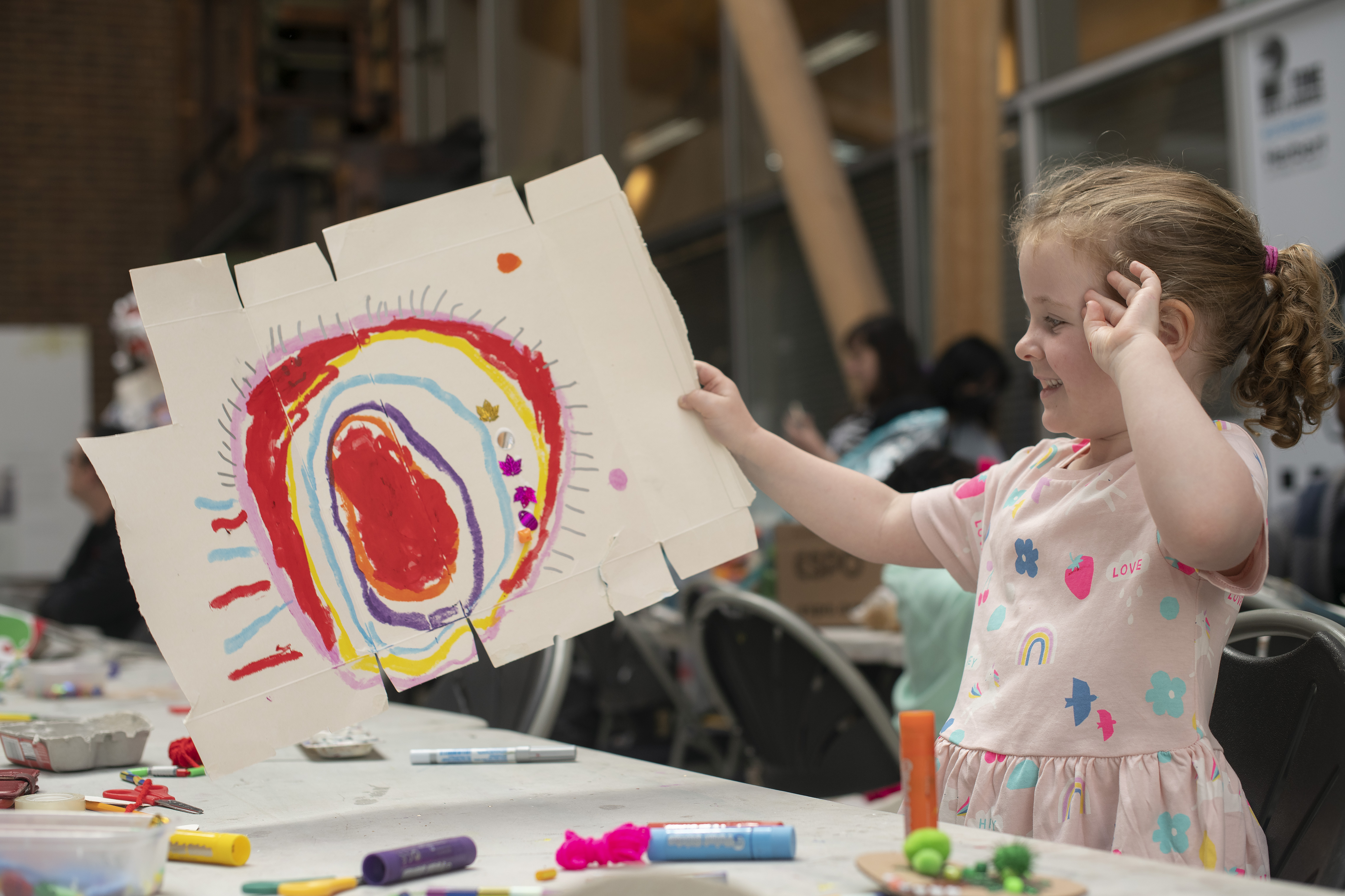 A girl holding up a brightly coloured, abstract drawing she has made on a piece of card
